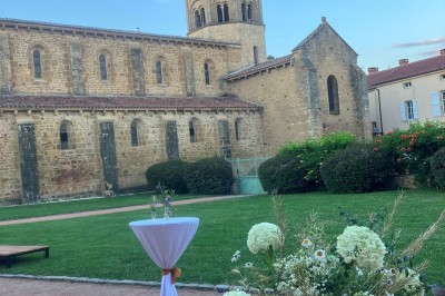 Église illuminée de nuit avec un clocher éclairé, vue depuis une allée avec des braseros allumés au premier plan.