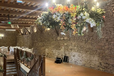 Église illuminée de nuit avec un clocher éclairé, vue depuis une allée avec des braseros allumés au premier plan.