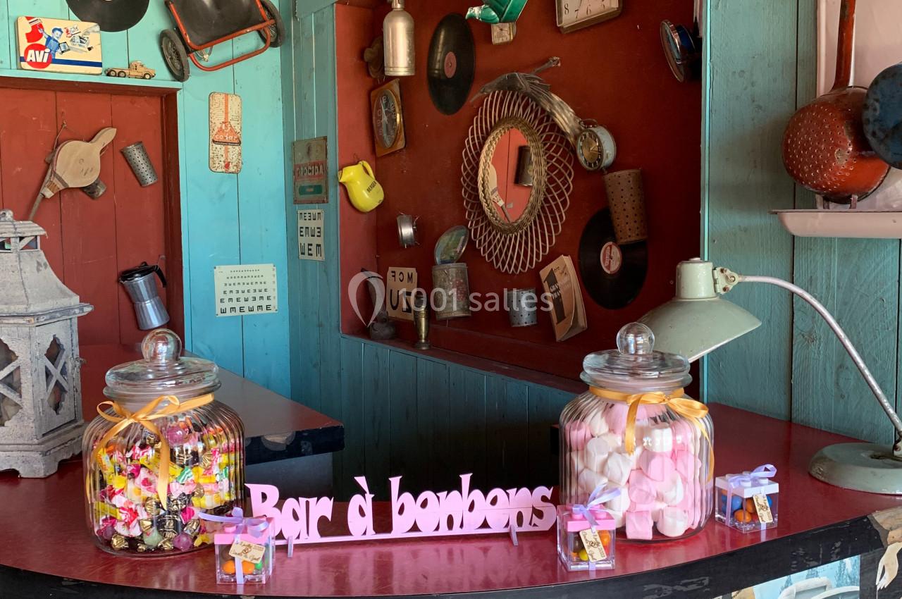 Bar à bonbons rétro avec pots remplis de sucreries colorées, décor vintage avec affiches et objets anciens.