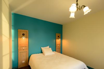 Lit double avec drap blanc, encadré par deux tables de chevet et lampes, dans une chambre au mur bleu et sol en bois.