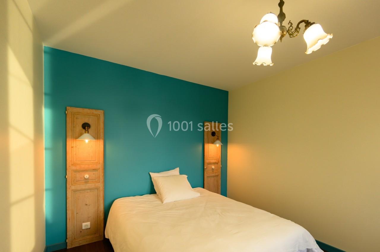 Chambre avec un lit simple, mur bleu, deux appliques murales et un plafonnier à trois abat-jours blancs.