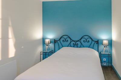 Lit double avec drap blanc, encadré par deux tables de chevet et lampes, dans une chambre au mur bleu et sol en bois.