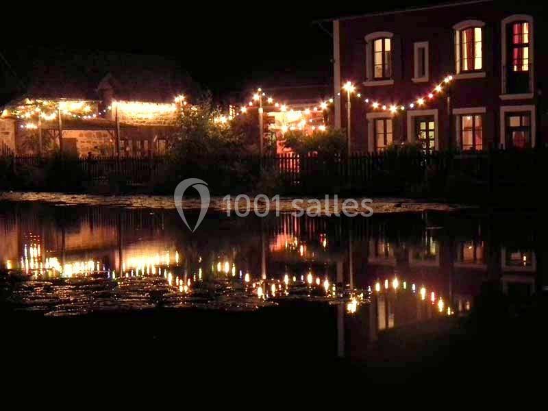 Façades éclairées et guirlandes lumineuses se reflétant dans l'eau calme d'un étang, de nuit.