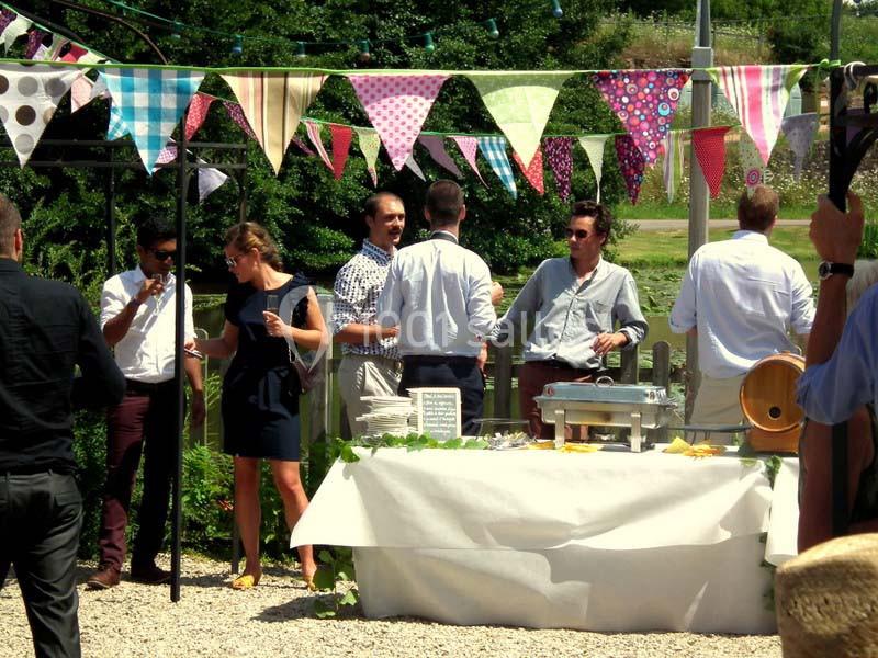 Des personnes discutent près d'une table de buffet en extérieur, décorée de fanions colorés.