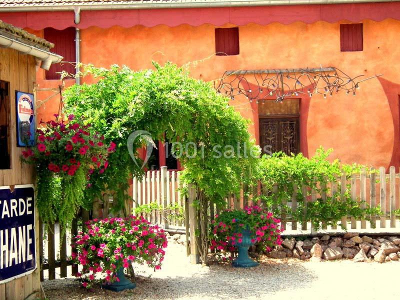 Arche végétale ornée de fleurs roses devant une maison aux murs orange avec une clôture en bois.