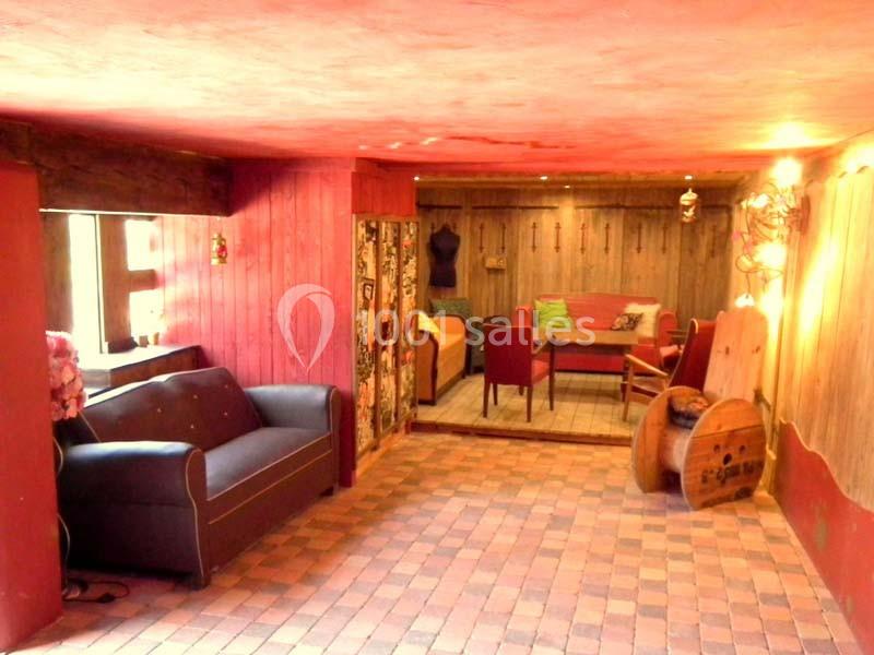 Salle chaleureuse avec murs rouges, sol en briques, canapé, fauteuils et décoration rustique en bois.