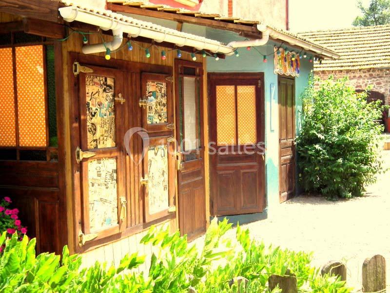 Façade colorée de petites boutiques en bois avec volets décorés, entourée de plantes et éclairée par des guirlandes.