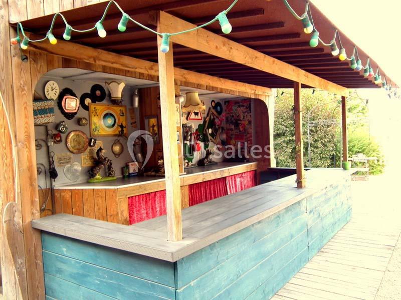 Comptoir en bois sous un auvent, décoré d'objets vintage et entouré de guirlandes lumineuses colorées.