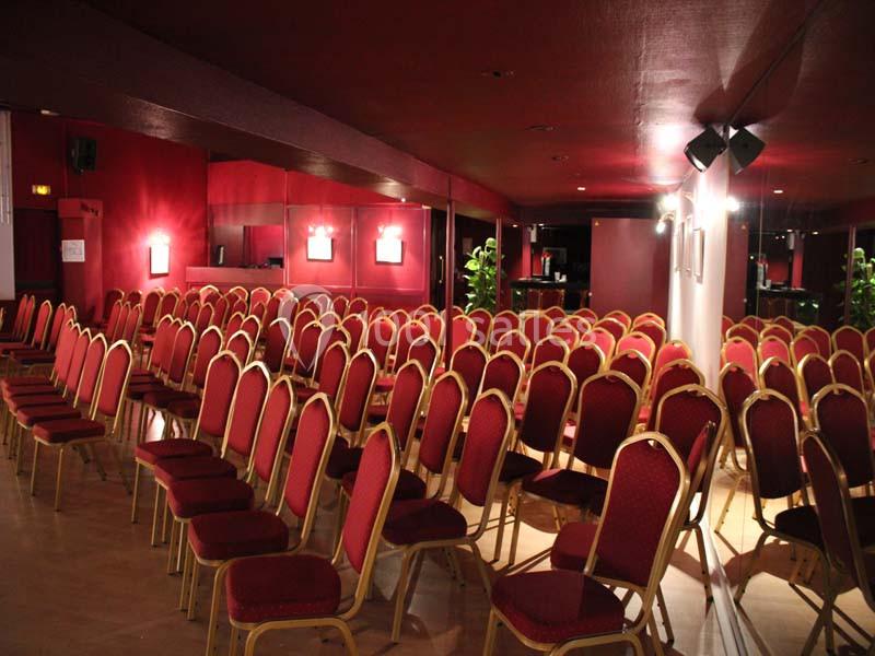 Salle de conférence avec des rangées de chaises rouges alignées devant des murs rouges et des miroirs.