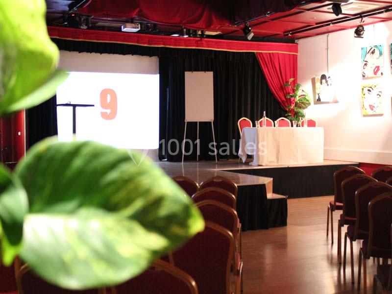 Salle de conférence avec des chaises alignées, une scène équipée d'un pupitre, d'un écran et d'une table drapée.