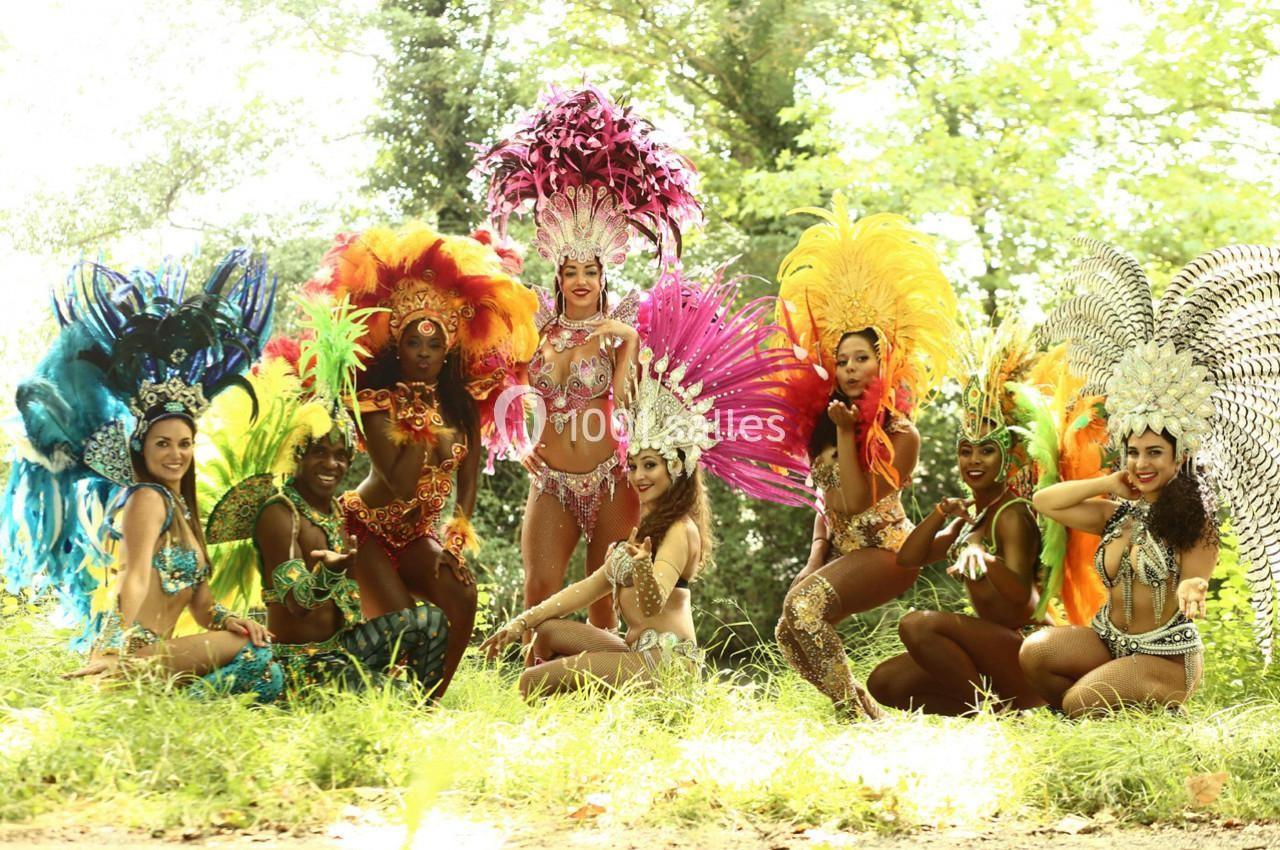 Un groupe de danseuses en costumes colorés et ornés de plumes posant dans un cadre naturel verdoyant.