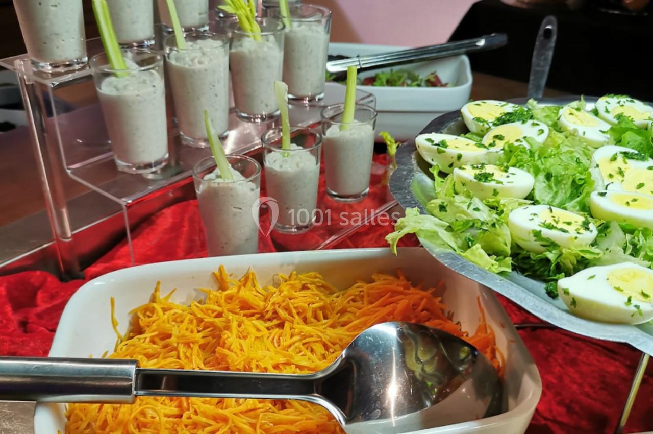 Buffet avec verrines de soupe, œufs durs sur salade verte et carottes râpées dans un plat blanc.