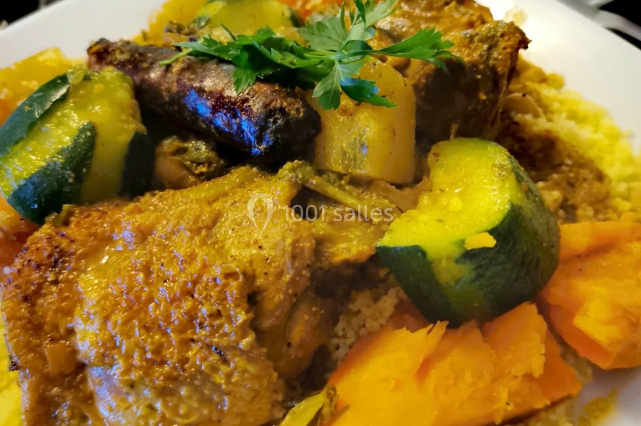 Plat de couscous avec légumes variés, morceaux de viande, merguez et herbes fraîches sur un lit de semoule.