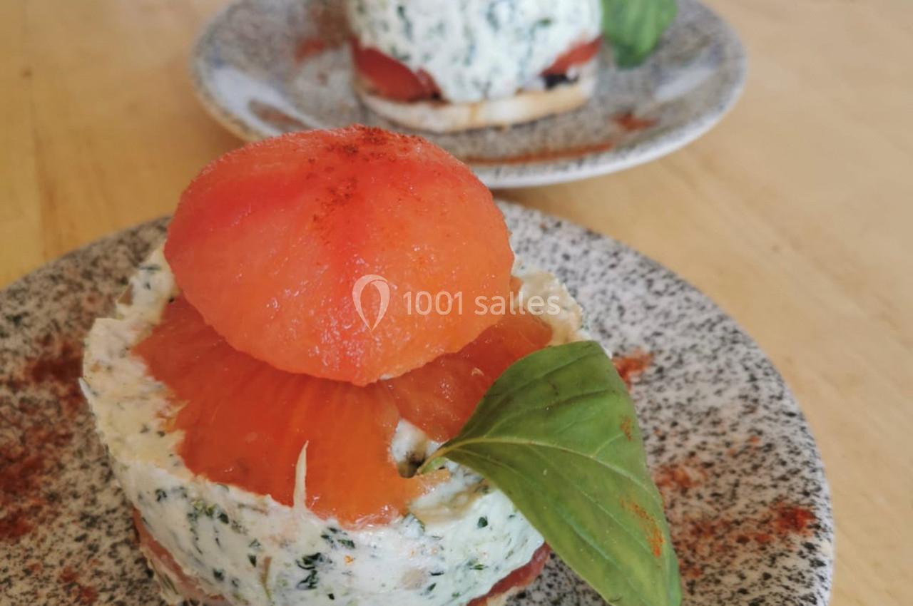 Entrée composée de fromage frais aux herbes, tranches de tomate et basilic, présentée en couches sur une assiette.