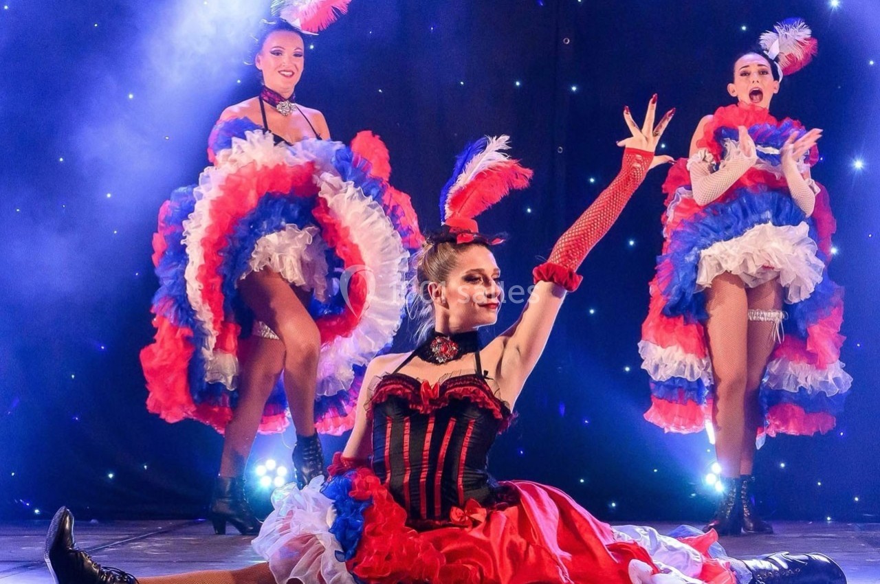 Danseuses de cabaret en costumes colorés rouge, blanc et bleu, exécutant une chorégraphie sur une scène éclairée.