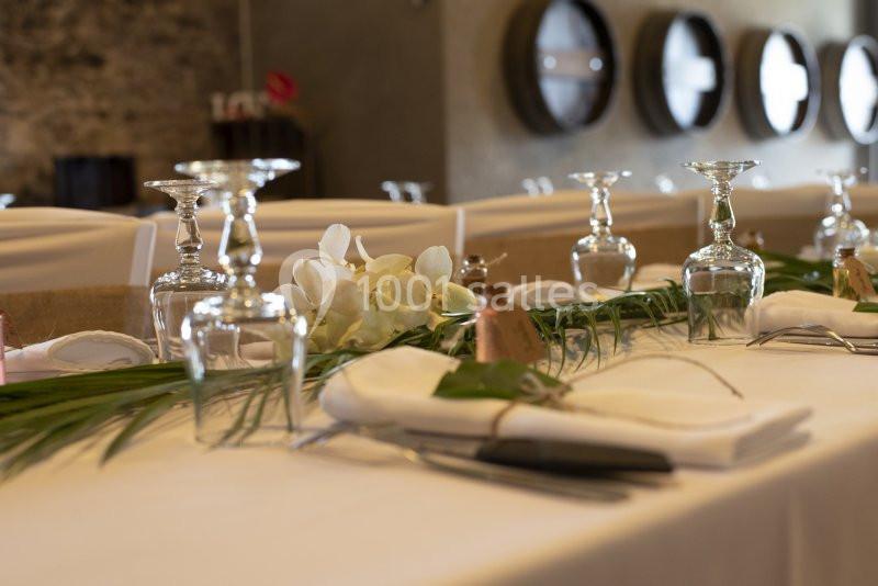 Table élégamment dressée avec nappes blanches, verres, couverts et décoration florale dans un cadre chaleureux.