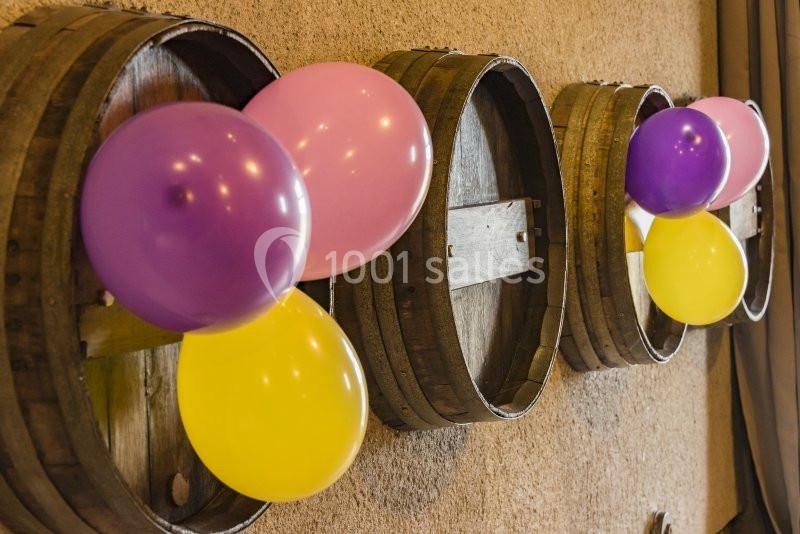 Des ballons colorés fixés sur des tonneaux en bois alignés contre un mur beige.