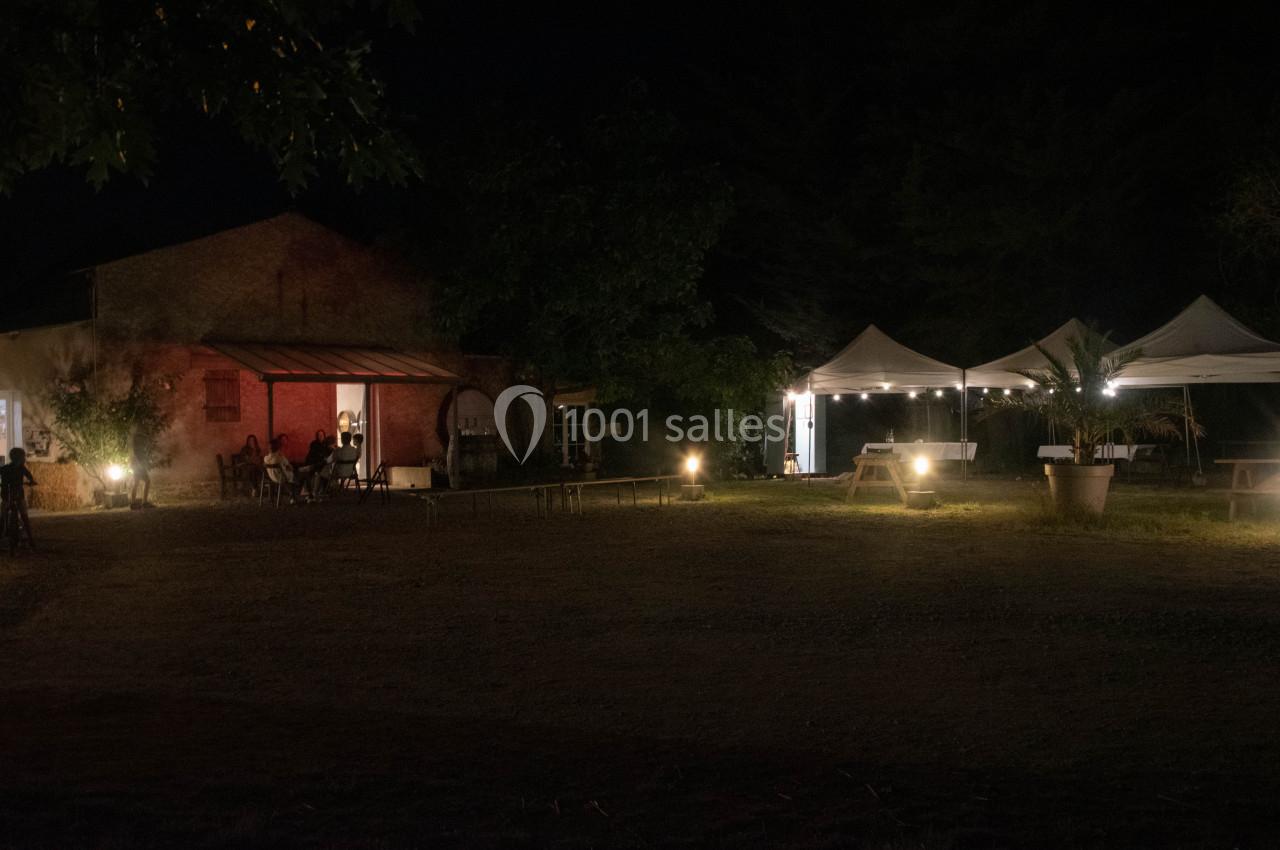 Cour extérieure éclairée la nuit avec des tentes blanches, des lumières et un bâtiment en arrière-plan.