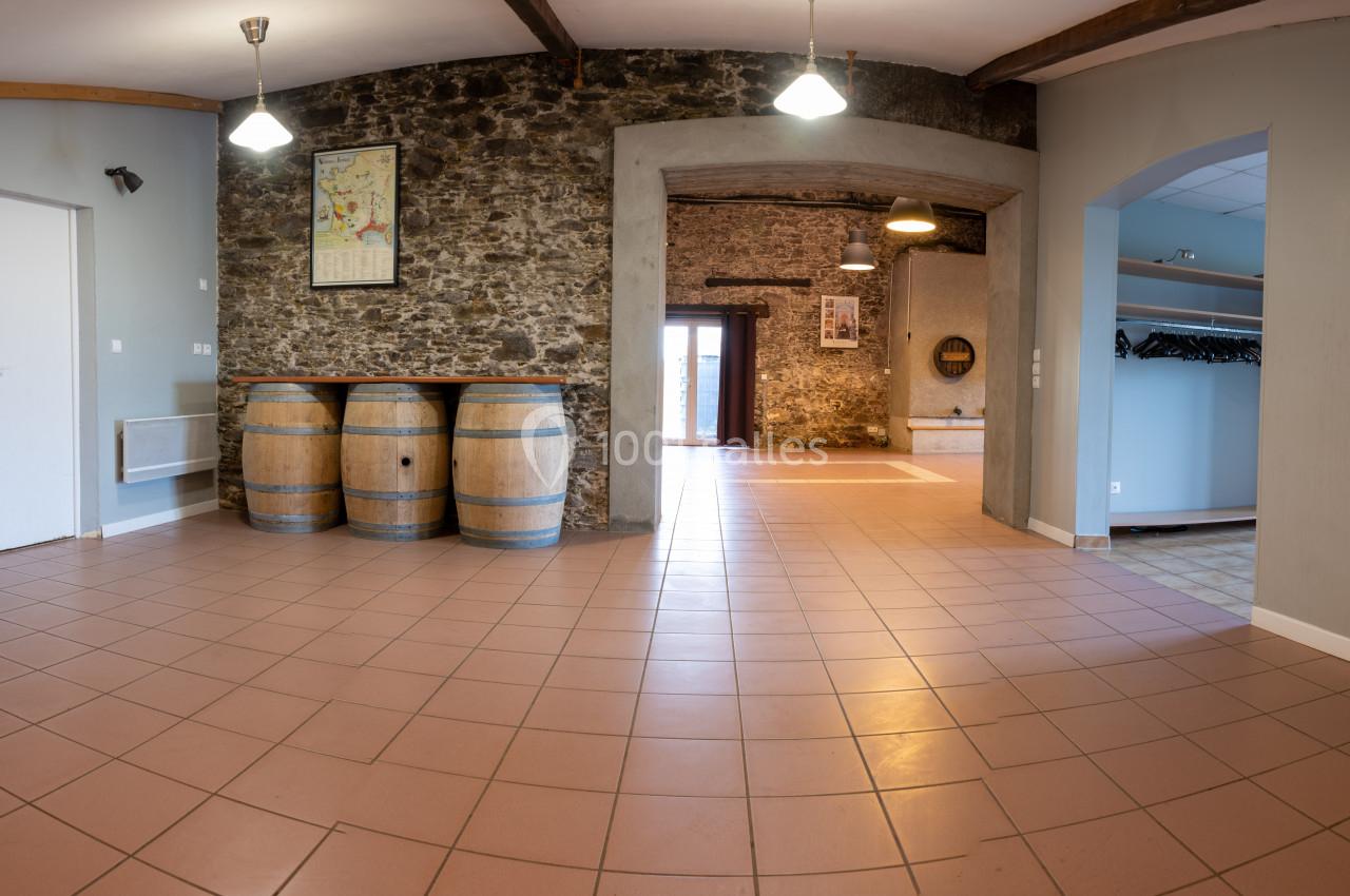 Salle intérieure avec murs en pierre, barriques en bois, carrelage au sol et éclairage suspendu.