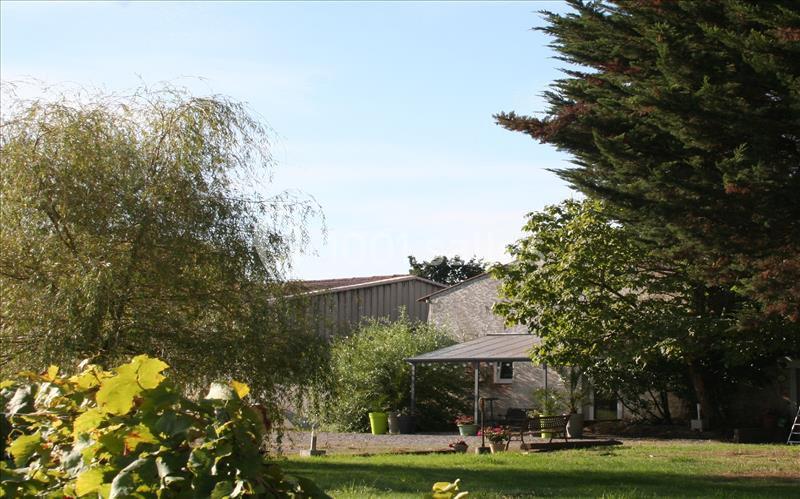 Vue d'un jardin avec pelouse, arbres, arbustes et une maison en arrière-plan sous un ciel dégagé.