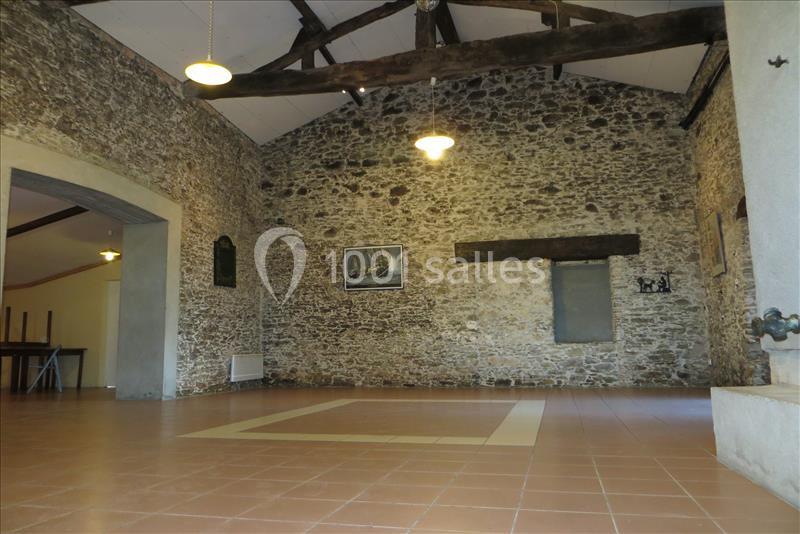 Salle intérieure avec murs en pierre apparente, poutres en bois, carrelage au sol et quelques décorations murales.