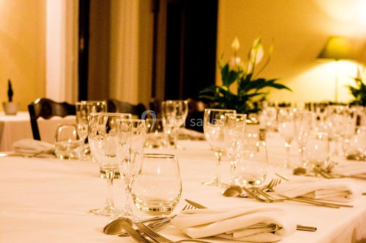 Table dressée avec nappes blanches, verres, couverts et serviettes, dans une salle éclairée par une lumière chaude.