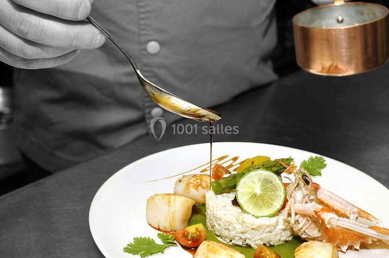 Un chef verse une sauce sur un plat raffiné composé de riz, fruits de mer, légumes et citron vert.