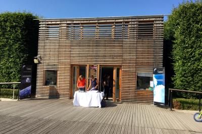 Façade en bois éclairée par des lumières violettes, avec une terrasse en bois et un grand parasol.