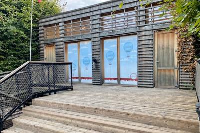 Façade en bois éclairée par des lumières violettes, avec une terrasse en bois et un grand parasol.