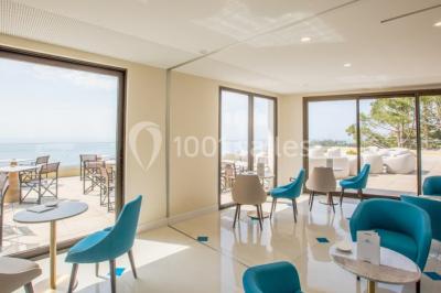 Terrasse ensoleillée avec tables hautes dressées, vue sur la mer et des arbres en arrière-plan.