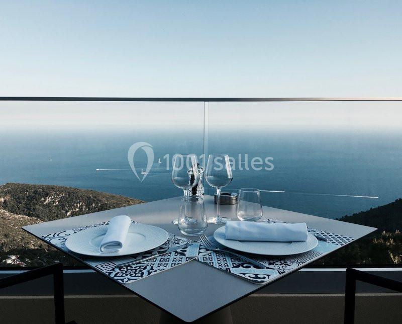 Table dressée avec vaisselle et verres, vue panoramique sur la mer et le ciel dégagé en arrière-plan.