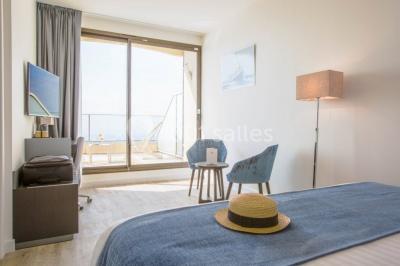 Terrasse ensoleillée avec tables hautes dressées, vue sur la mer et des arbres en arrière-plan.