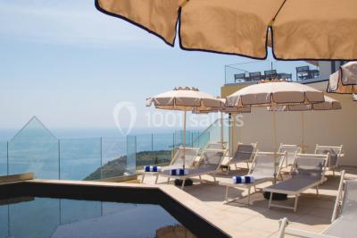 Terrasse ensoleillée avec tables hautes dressées, vue sur la mer et des arbres en arrière-plan.