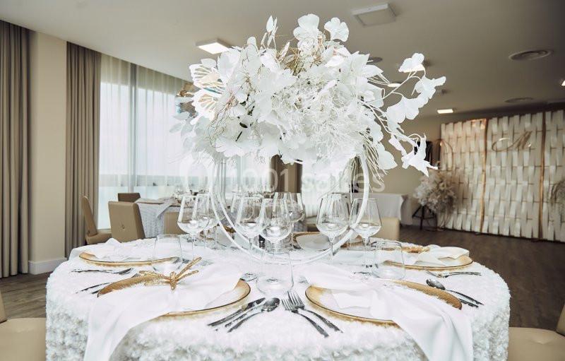Table élégamment dressée avec une nappe blanche, des couverts raffinés et un grand centre de table floral blanc.