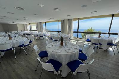 Terrasse ensoleillée avec tables hautes dressées, vue sur la mer et des arbres en arrière-plan.