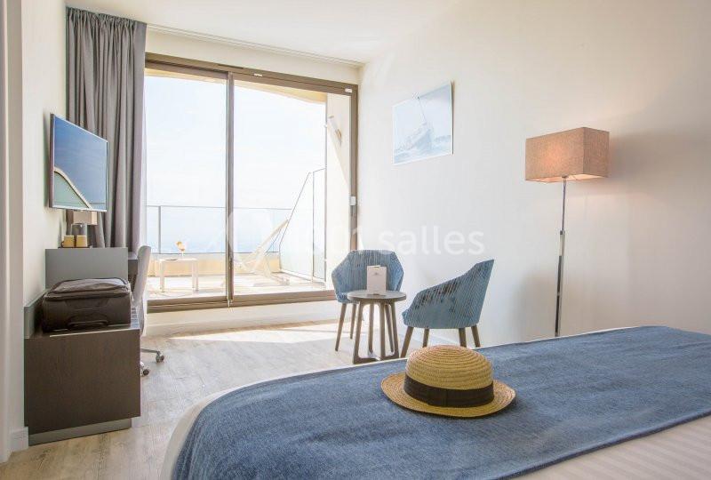 Chambre lumineuse avec lit, table, chaises, télévision et balcon offrant une vue dégagée sur l'extérieur.