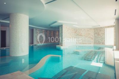 Salle de réunion lumineuse avec tables disposées en U, chaises blanches, bouteilles d'eau et écran de projection.