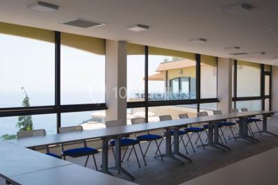 Salle de réunion lumineuse avec tables disposées en U, chaises blanches, bouteilles d'eau et écran de projection.