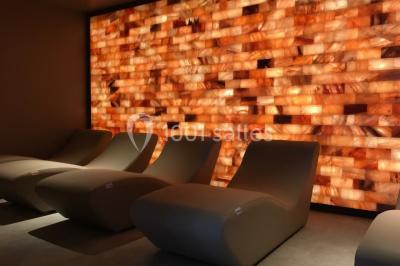 Salle de réunion lumineuse avec tables disposées en U, chaises blanches, bouteilles d'eau et écran de projection.