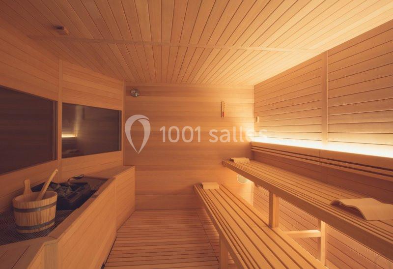 Intérieur d'un sauna en bois clair avec bancs, seau en bois et lumière douce.