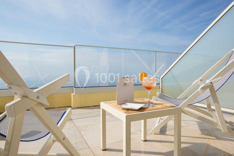 Deux chaises longues blanches sur une terrasse avec vue dégagée, table avec cocktail et menu au centre.