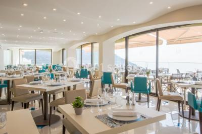 Salle de réunion lumineuse avec tables disposées en U, chaises blanches, bouteilles d'eau et écran de projection.