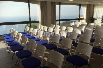 Salle de réunion lumineuse avec tables disposées en U, chaises blanches, bouteilles d'eau et écran de projection.