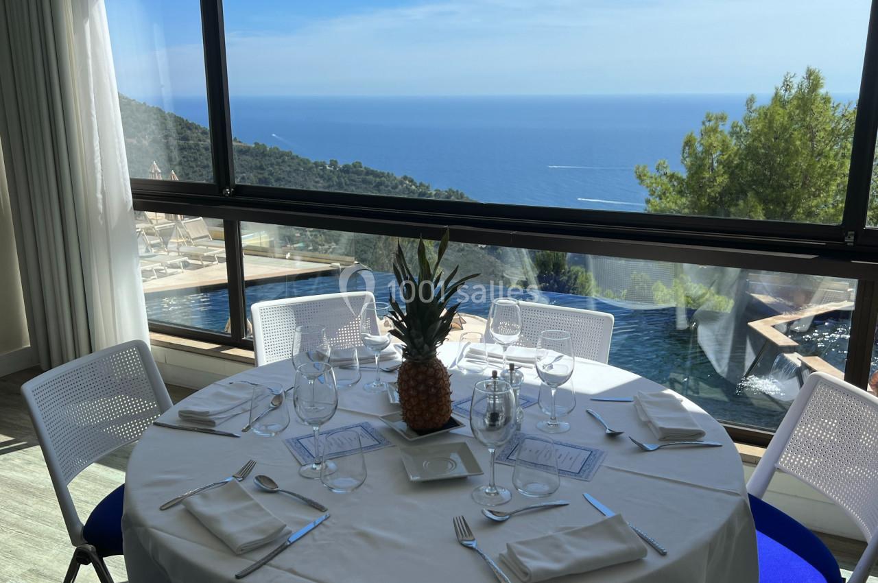 Table dressée avec vue panoramique sur la mer, entourée de baies vitrées et d'une piscine extérieure.