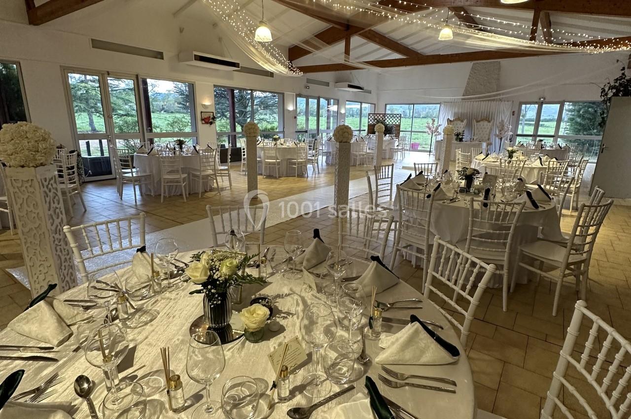Salle de réception lumineuse avec tables élégamment dressées, chaises blanches et décorations suspendues.