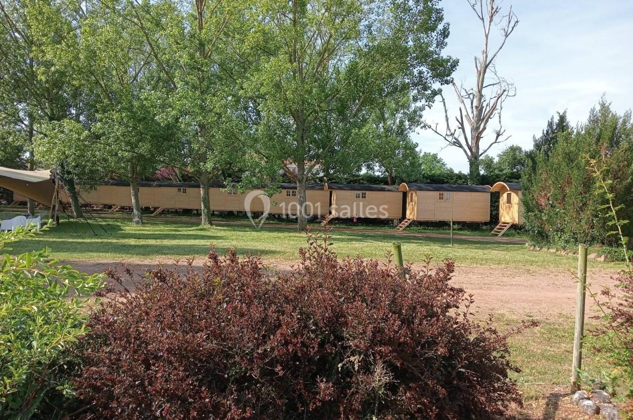 Alignement de roulottes en bois dans un espace verdoyant entouré d'arbres et de buissons.