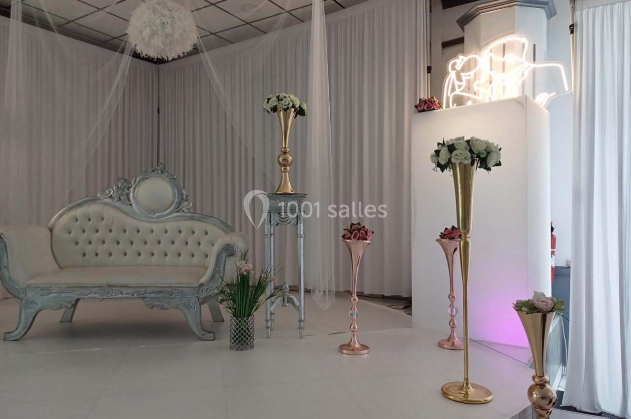 Salle décorée pour un événement avec canapé capitonné, colonnes dorées et arrangements floraux.