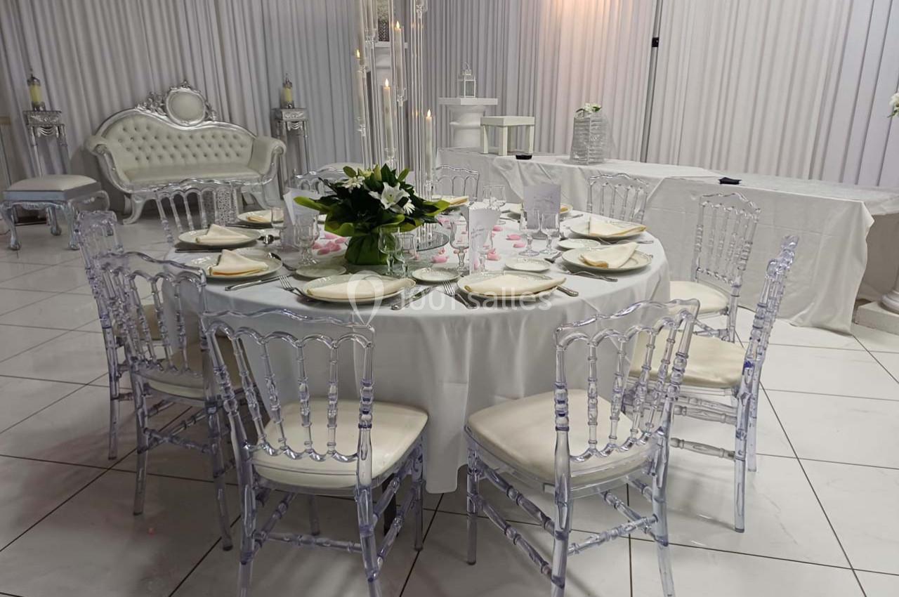 Table ronde élégamment dressée avec des chaises transparentes, des assiettes blanches et un centre de table floral.