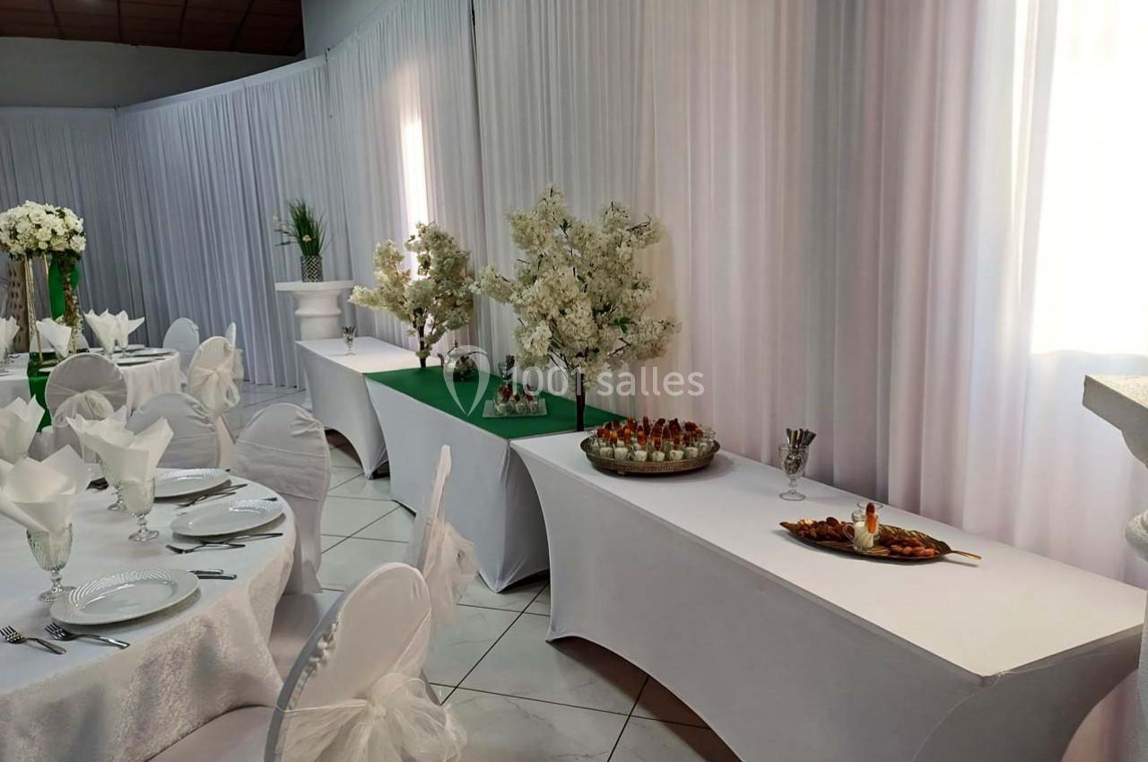 Salle de réception décorée avec des tables dressées, nappes blanches et buffets ornés de fleurs blanches.