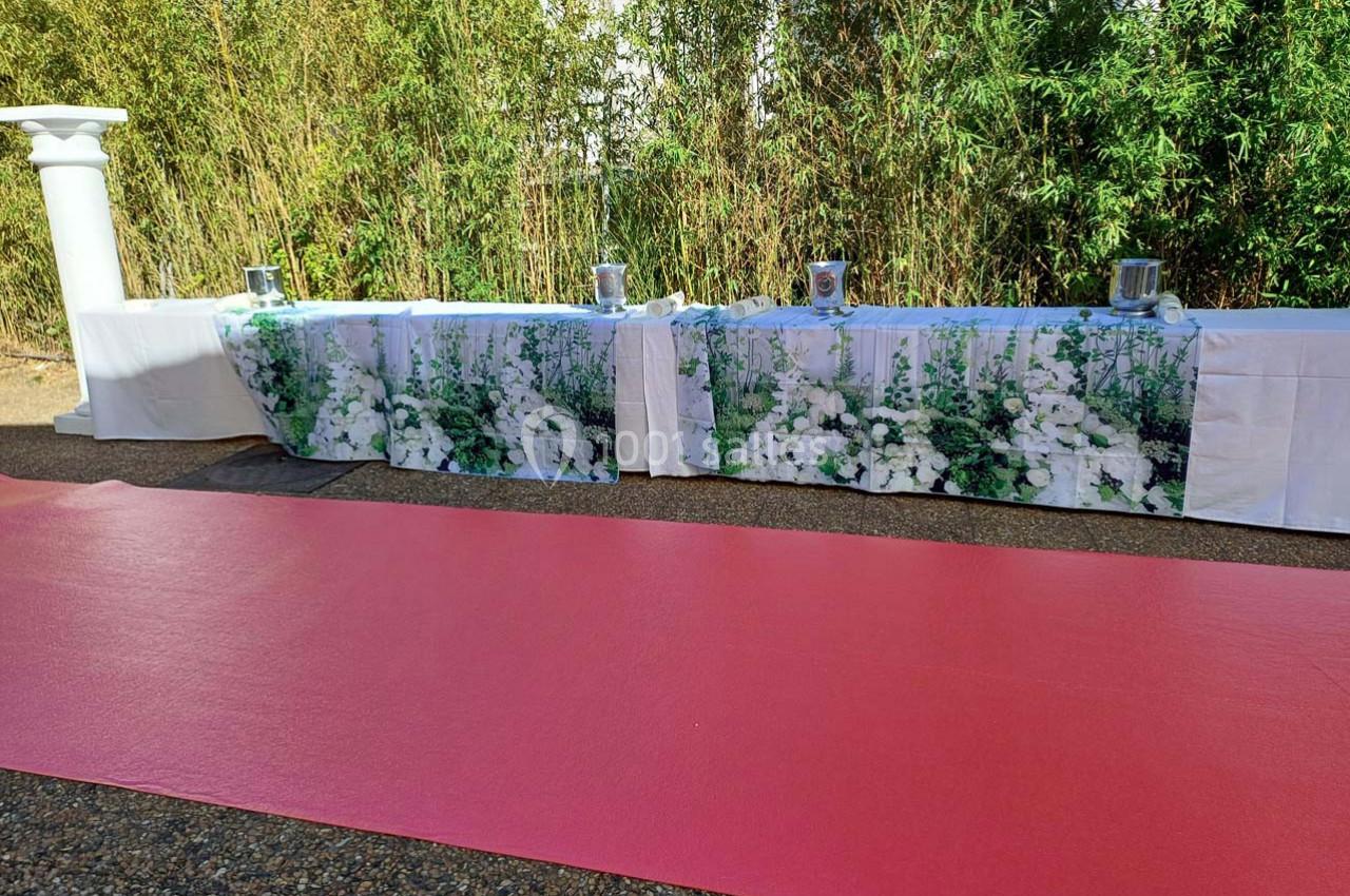 Tables décorées de nappes à motifs floraux blancs, alignées devant un tapis rouge et des bambous en arrière-plan.